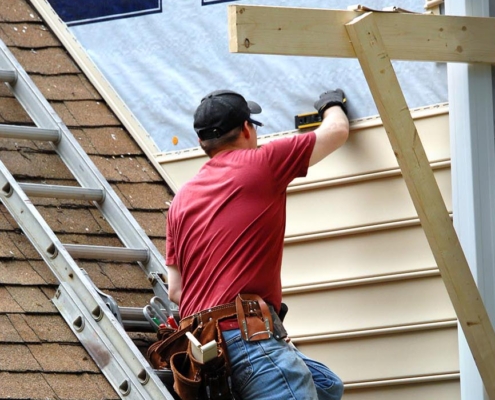 Worker installing siding on house